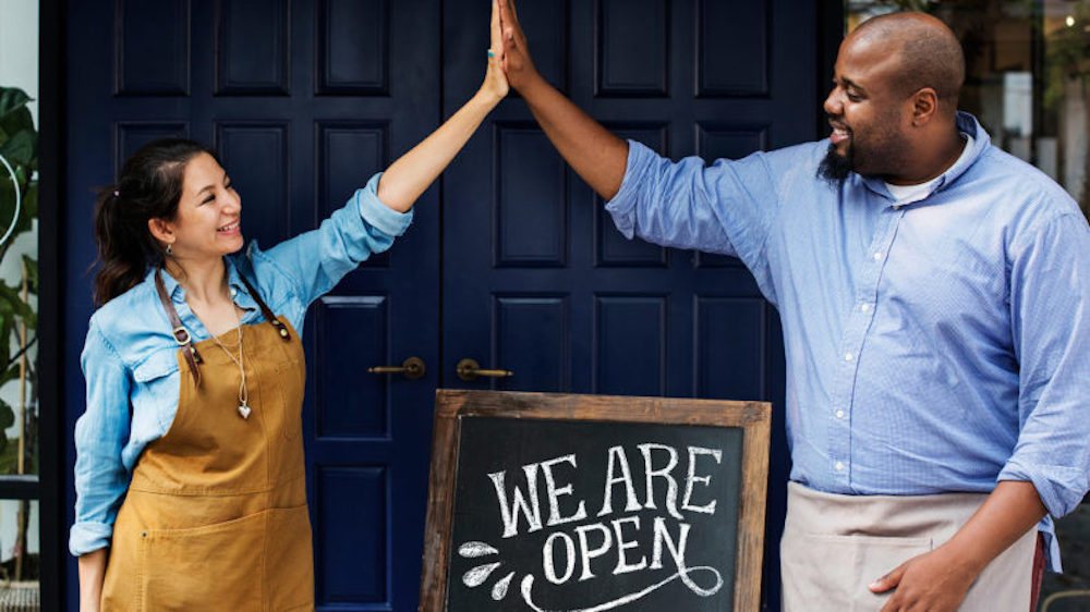 Two small-business owners celebrating outside their newly opened shop.
